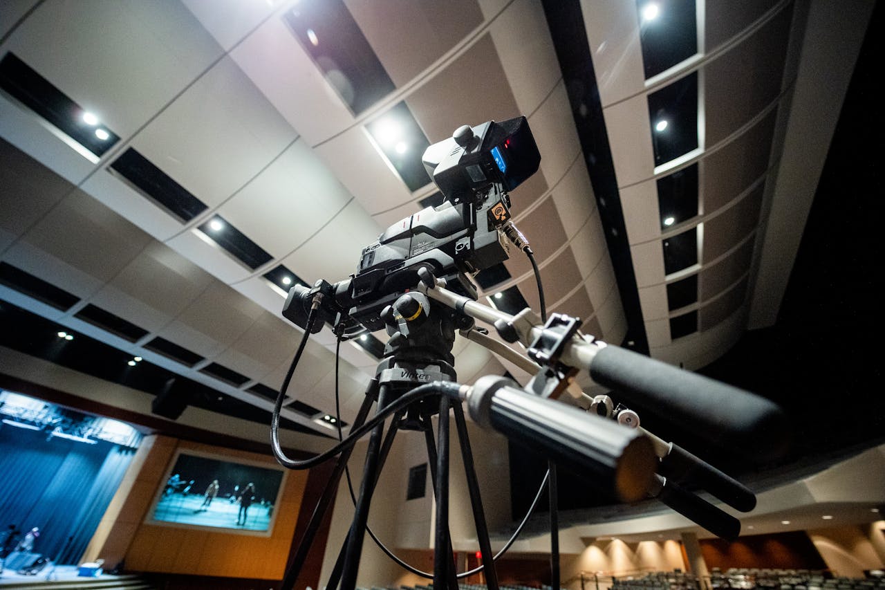Low angle of modern professional video camera on tripod placed near stage under ceiling with glowing lights